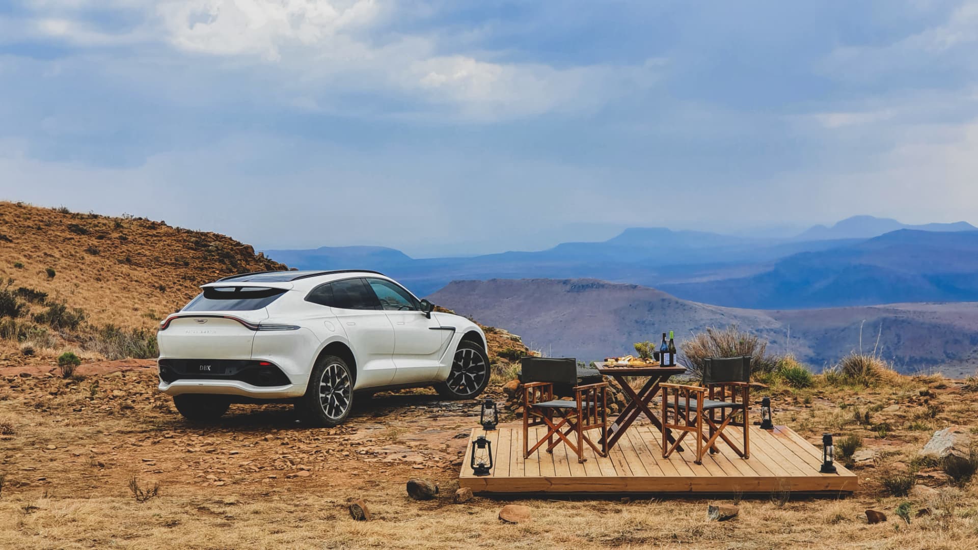 White Aston Martin DBX beside an outdoor table overlooking the Karoo mountains