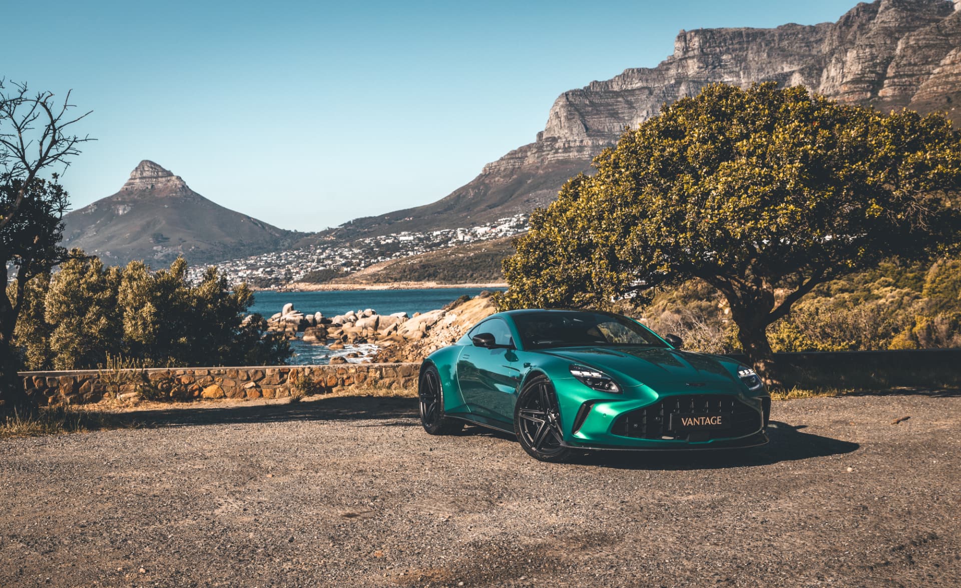 Green Aston Martin Vantage parked beside the Cape Town coastline and mountains