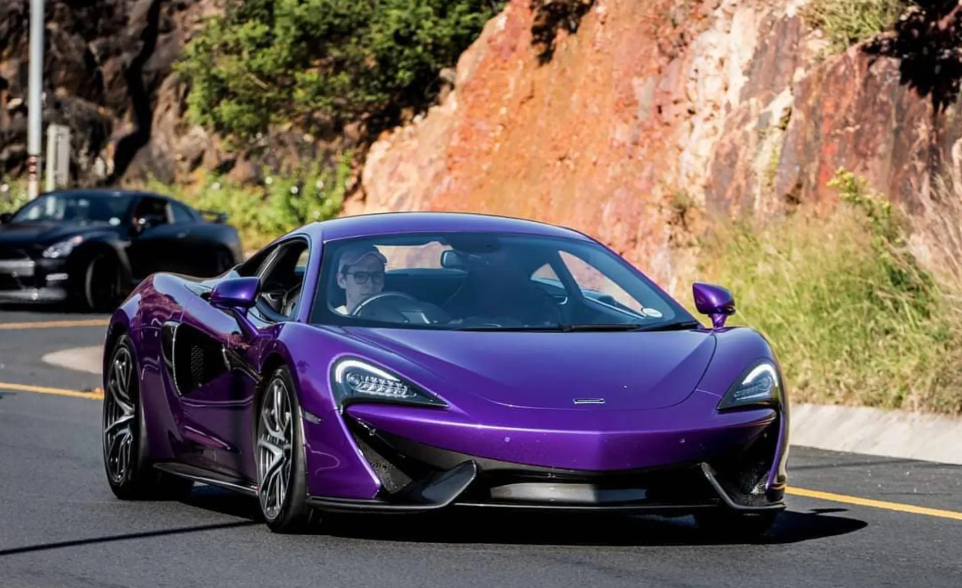 Purple McLaren driving through a mountain pass with a black performance car behind