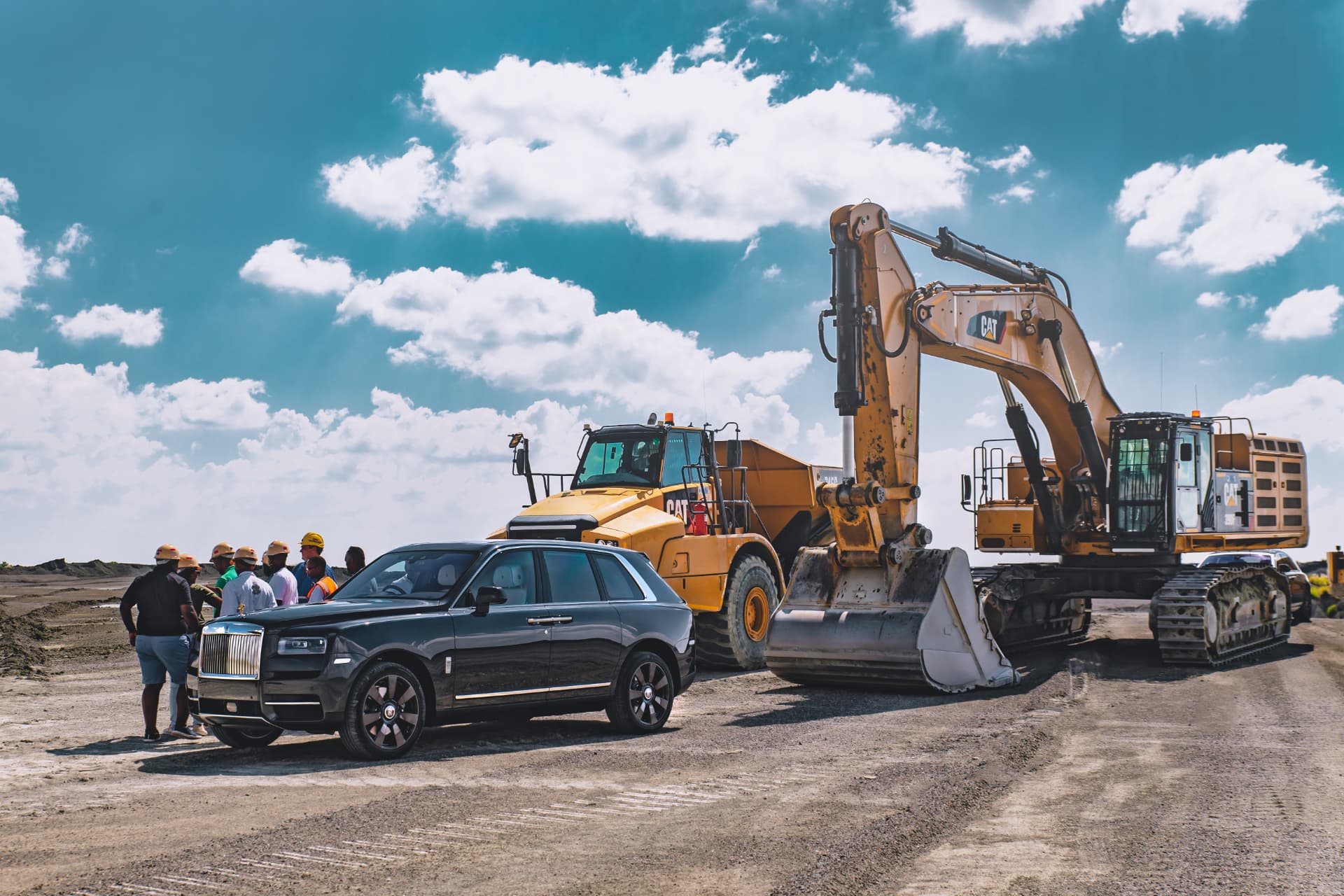 Black Cullinan beside a CAT excavator and dump truck with guests on the mine floor