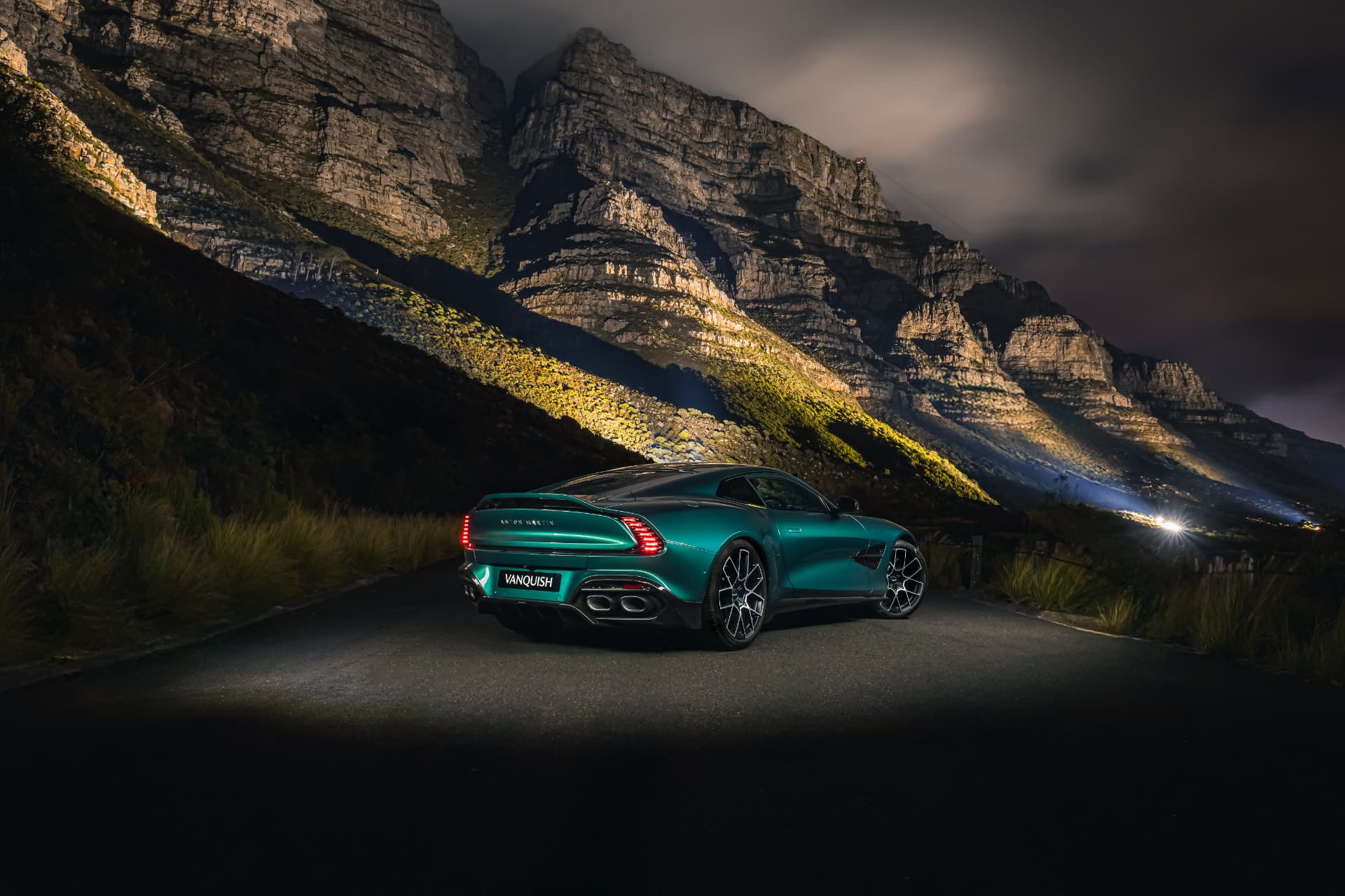 Green Aston Martin Vanquish illuminated beneath the Twelve Apostles at night
