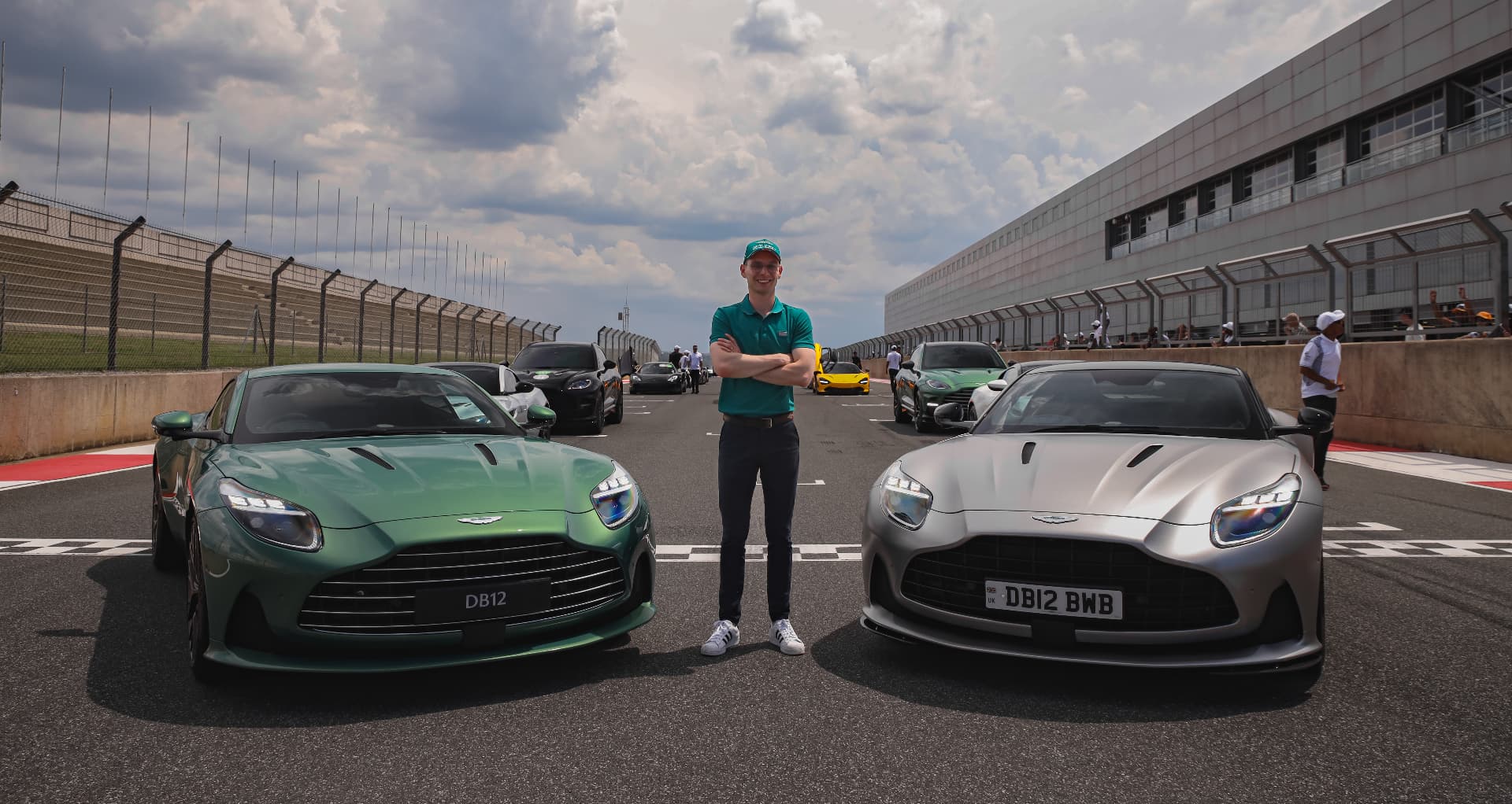 Man standing between a green and a silver DB12 on a start line