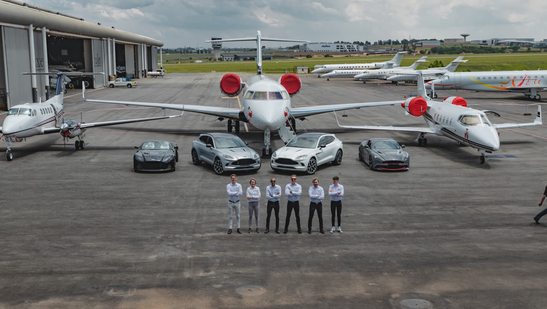 Aston Martin fleet and team lined up in front of a private jet on the ExecuJet apron at Lanseria