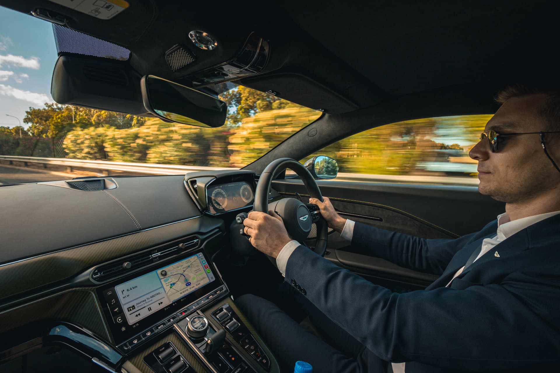 Driver at the wheel of an Aston Martin Vantage viewed from the passenger seat
