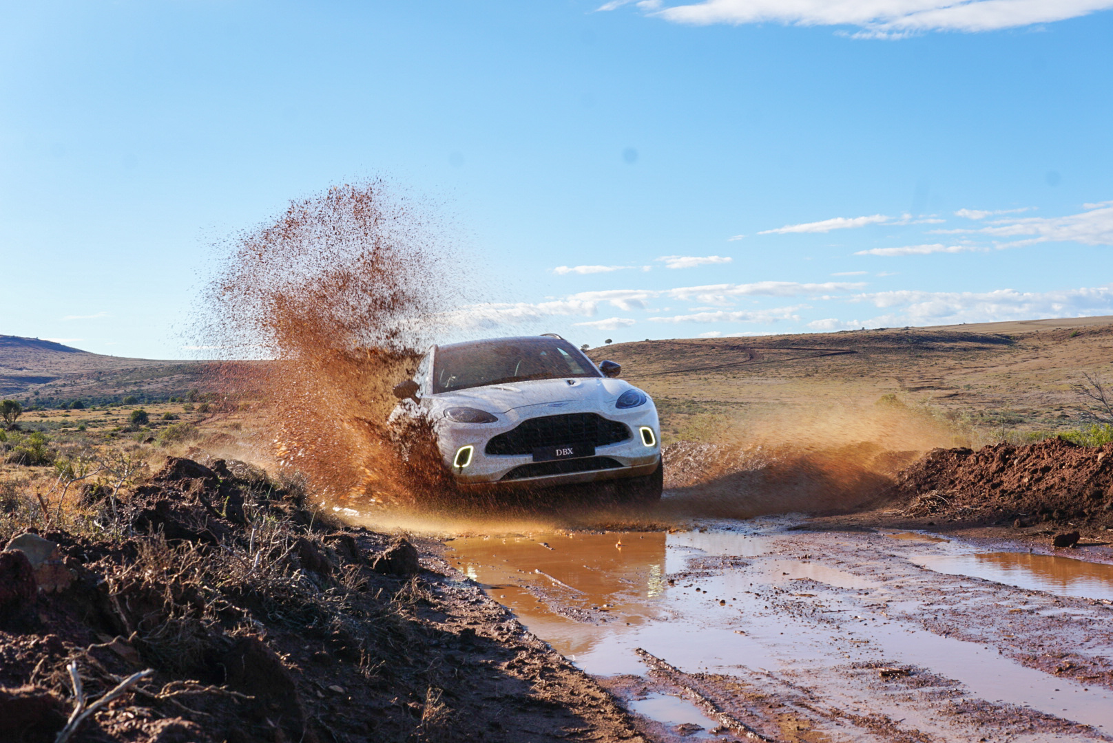 White DBX throwing mud through a puddle on a dirt track in the Karoo