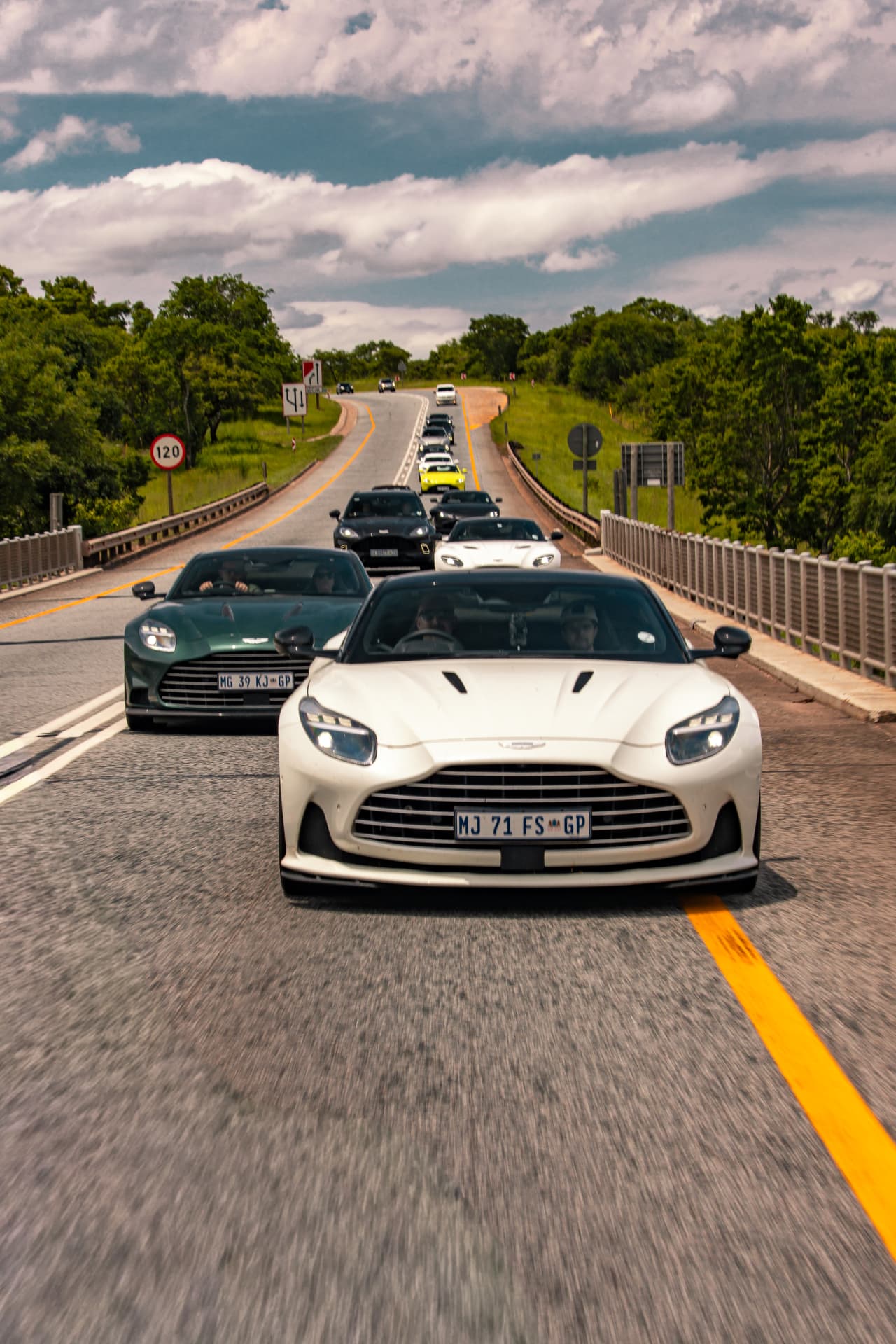 White DB12 Volante leading the Escape Tour convoy over a bridge with a green Vanquish alongside